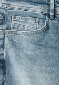 Jeans de mezclilla azul claro con un pequeño bolsillo frontal, costuras visibles y una textura suave con patrones de desgaste ligeros.