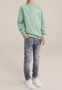 Světle zelená mikina s žebrovanými manžetami a kulatým výstřihem, s bílým textem "ATLANTA". V kombinaci s úzkými šedými džíny a bílými teniskami.