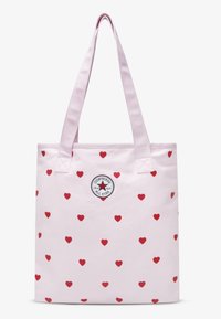 Τσάντα ώμου σε ανοιχτό ροζ χρώμα με κόκκινα σχέδια καρδιάς και στρογγυλό ασπρόμαυρο λογότυπο Converse. Διαθέτει ανθεκτικές ροζ λαβές για φορητότητα.