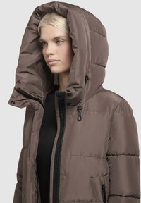 Rjav napihnjen plašč z velikim, izoliranim kapuco, zadrgo spredaj in stranskimi žepi. Gladka tekstura z oblazinjenjem v obliki diamanta.
