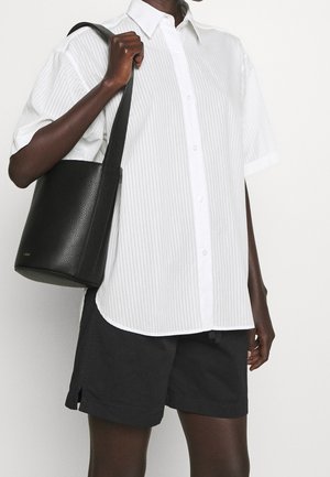 White striped short-sleeve shirt with a button front, paired with black shorts. The person carries a black leather bucket bag.