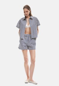 Camisa de manga corta a rayas y pantalones cortos a juego en azul y blanco. La camisa cuenta con un cuello y un bolsillo; los pantalones cortos tienen un cinturón. Tejido ligero.