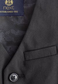 Blazer en tissu noir avec une texture lisse, doté d'une poche poitrine, d'une fermeture à un bouton et d'une doublure à motifs étiquetée "next."