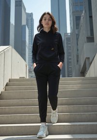 Fekete kapucnis pulóver elől zsebből és barna címkéből, passzoló melegítőnadrággal párosítva. Fehér sportcipők, sima anyag, laza fazon és minimalista dizájn.
