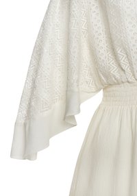 Abito bianco con un corpino in pizzo testurizzato con motivi geometrici, maniche ampie e vita arricciata, realizzato in un tessuto leggero.