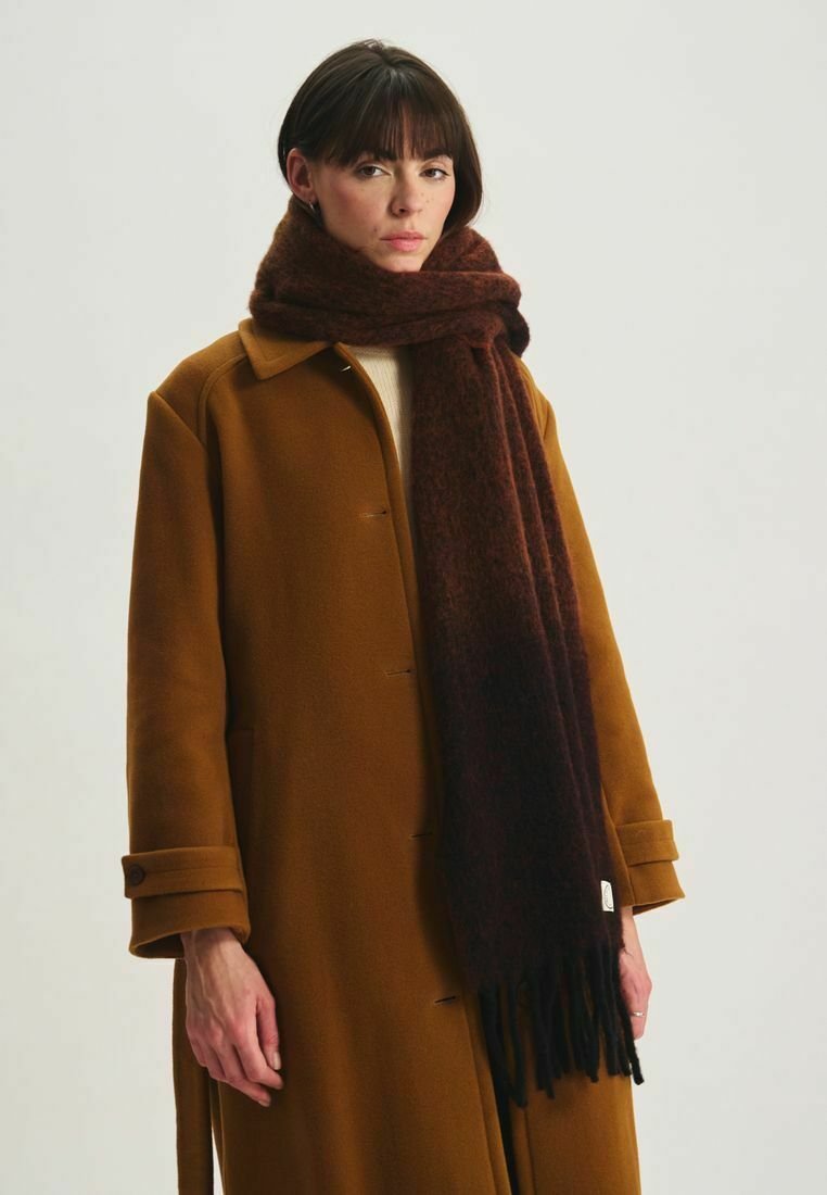 Écharpe en laine marron avec une texture douce et des franges, portée sur un manteau camel, présentant un design ajusté et des accents de boutons.