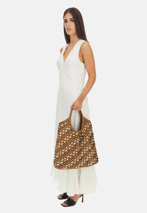 Borsa tote intrecciata marrone con accenti bianchi, dotata di un manico rotondo, abbinata a un vestito bianco senza maniche e sandali neri aperti sul davanti.