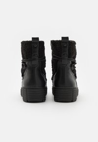 Botas negras hasta el tobillo con cuerpo de cuero suave y un cuello de textil suave. Presentan una suela texturizada y un diseño de cordones con una lengüeta en la parte posterior.
