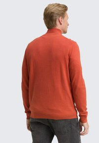 Pull à col roulé en tricot de couleur orange vif, avec des poignets et un ourlet côtelés, vu de dos. Texture douce et coupe légèrement ajustée.