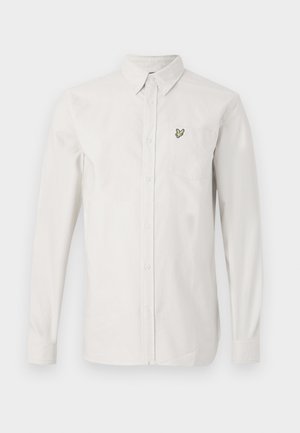 Chemise blanche à boutons en coton avec des manches longues. Présente un petit logo d'oiseau brodé en vert sur la poche poitrine gauche.