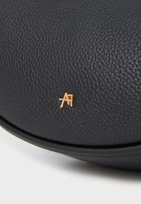 Artigo em couro texturizado preto com um logótipo metálico dourado apresentando letras entrelaçadas "A" e "A" em destaque.