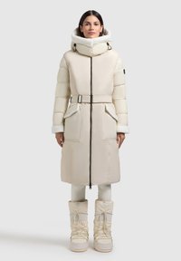 Lange puffer coat in off-white, met een ceintuurlijn in de taille, hoge kraag en een hoodie met bontvoering. Gecombineerd met bijpassende, gevoerde snowboots.