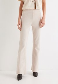 Beige uitlopende broek gemaakt van zachte stof met een gladde textuur, hoge tailleband en een aansluitende pasvorm tot aan de zoom.