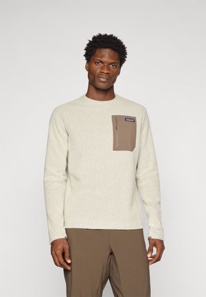Pullover sweater in light beige with a textured knit pattern. Features a brown chest pocket with a zipper and a brand logo. Long sleeves.