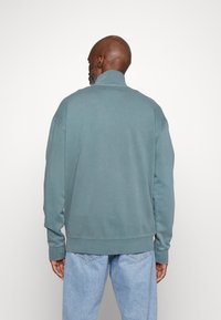 Lichtblauwe sweatshirt met een hoge kraag, ribgebreide manchetten en zoom, met een ontspannen pasvorm en zachte, gestructureerde stof. Achteraanzicht getoond.