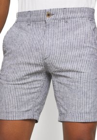 Modré a bílé pruhované šortky vyrobené z lehkého materiálu, s knoflíkovým zapínáním, bočními kapsami a přizpůsobeným střihem.