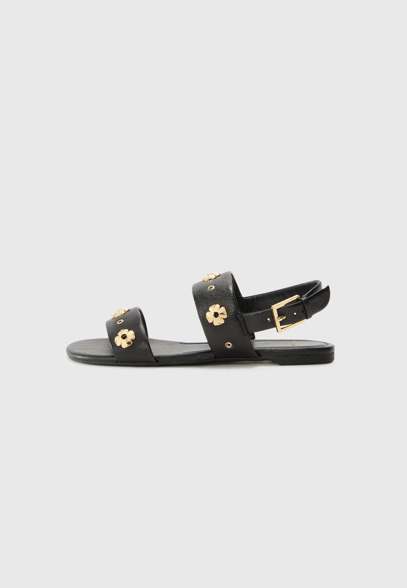 Black leather sandals with two wide straps, adorned with gold flower embellishments and adjustable ankle buckle. Flat sole.