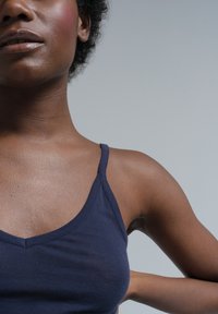 Navy blue tank top with thin straps, v-neck design, and smooth cotton texture. Close-up shows shoulder and upper arm detail.
