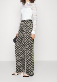 Haut blanc à manches longues avec détail transparent rayé, associé à un pantalon large à motif noir et blanc avec une bande latérale jaune.