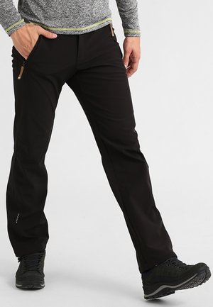 Homme portant un pantalon de plein air noir avec poches zippées, une chemise grise à manches longues et des chaussures de randonnée noires, debout avec un pied en avant.