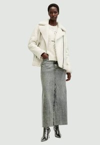 White shearling jacket with a wide collar, paired with a light knit sweater and a long grey denim skirt. Shiny black heeled boots complete the look.