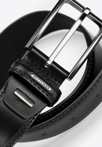 Cinturón de cuero negro con una hebilla de metal plateado en forma de delantería. El cinturón tiene una textura suave con detalles de costura y una etiqueta de marca grabada.