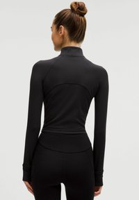 Langærmet sort atletisk top med ribbet tekstur, høj krave og tætsiddende design, parret med højtaljede sorte leggings.