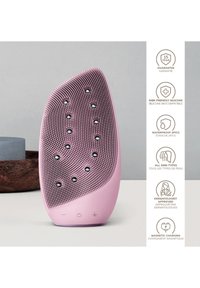 Dispositif de nettoyage facial en silicone de couleur rose pastel, avec une surface texturée et des accents noirs, conception étanche et port de charge magnétique.