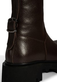 Bottines en cuir marron avec une finition texturée, semelle en caoutchouc robuste et une accent en boucle en métal sur le côté.