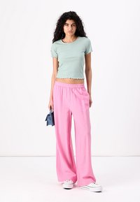 Top corto a righe verde chiaro abbinato a pantaloni rosa a gamba larga. L'outfit presenta un tessuto testurizzato con una vita elasticizzata.