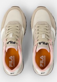 Baskets FILA avec un dessus en cuir beige et blanc, des accents roses, du cuir suédé texturé et une semelle intérieure orange rembourrée.