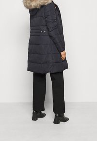 Marinblå puffjacka med en foder av päls i huvan, med horisontellt quiltad design, åtsittande midja och tryckknappsdetaljer. I kombination med svarta byxor och klackstövlar.