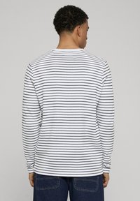 Wit shirt met lange mouwen en marineblauwe strepen. Voorzien van een ronde halslijn en een zachte textuur. Draagt een donkere blauwe jeans, gezien van achteren.