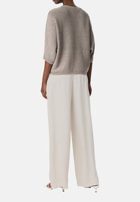 Maglione a maglia beige chiaro con maniche corte e dettagli di luccichio sottili, abbinato a pantaloni bianchi larghi realizzati in un tessuto fluido.