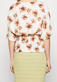 Kwiatowa bluzka w brzoskwiniowo-zielony wzór maków, lekki materiał, luźny krój i ściągnięta talia. Połączona z teksturowaną zieloną spódnicą.