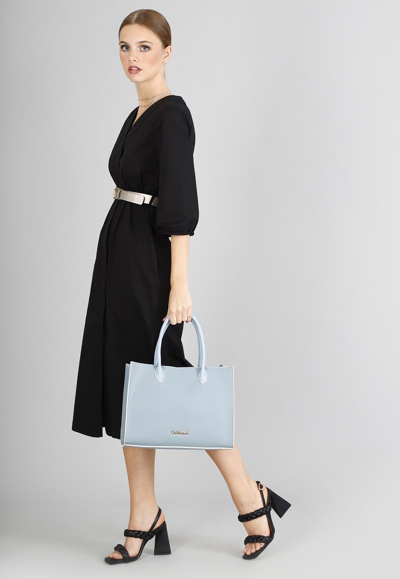 Borsa tote in pelle blu chiaro con doppie maniglie e cucitura a contrasto, abbinata a un vestito nero con maniche lunghe e una cintura metallica.