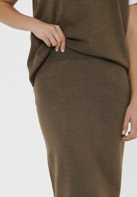 Rjav pleten top in krilo set, ki vsebuje rebrast rob in gladko teksturo, z oprijeto silhueto in usklajeno barvo skozi celotno oblačilo.