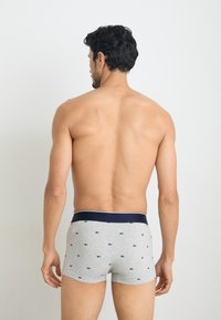 Boxer-briefs gris avec taille bleu marine, ornés d'un motif de petits logos bleu foncé. Le tissu semble être un mélange de coton, avec une texture lisse.