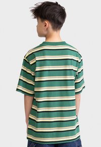 Green striped t-shirt with horizontal stripes in yellow, black, and cream colors; short sleeves and a crew neckline; relaxed fit.