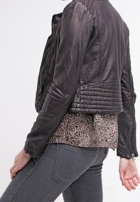 Sort læderjakke med quiltet rygdesign, båret over en beige leopardprint-top, parret med grå jeans. Glat tekstur og tætsiddende stil.