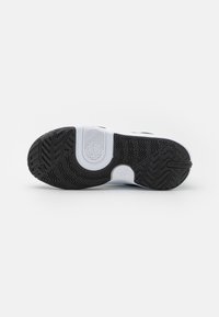 Semelle de sneaker noir et blanc avec des motifs de grip en caoutchouc texturé, présentant un accent blanc et un logo intégré dans le design.