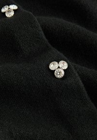 Black fabric with a soft texture, featuring three silver-tone crystal embellishments arranged in a triangular pattern.
