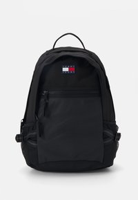 Mochila negra con un acabado de tela suave, que cuenta con un bolsillo frontal con cremallera, bolsillos laterales de malla y un parche con el logotipo en la parte superior.