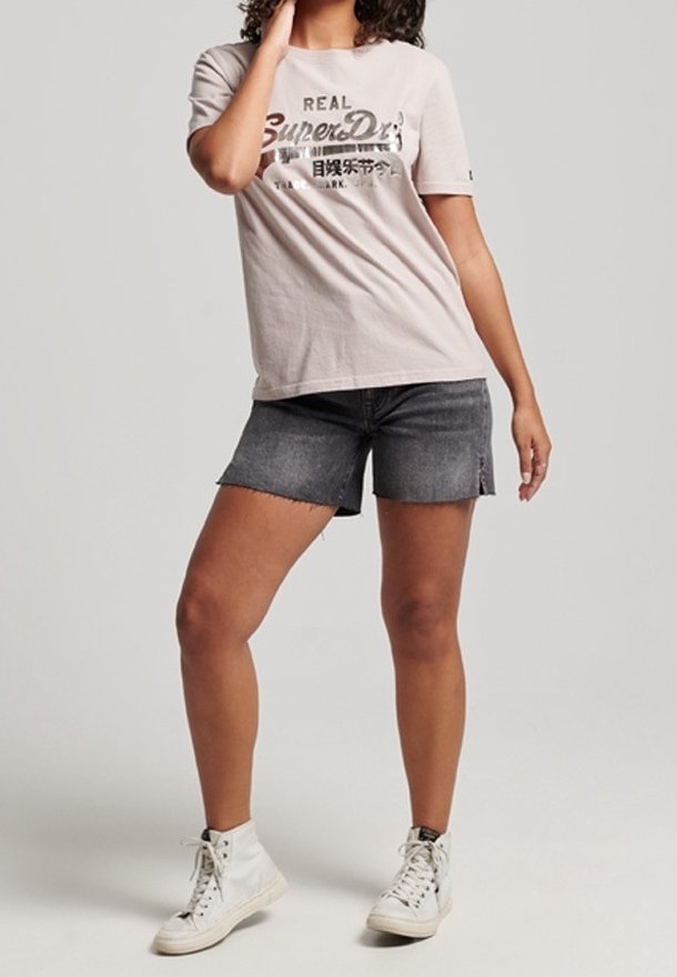 Světle šedé bavlněné tričko s grafikou "Superdry", doplněné o tmavé džíny šortky. Model má na sobě bílé vysoké tenisky. Jednoduchý design.