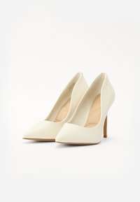 Valkeat korkokengät, joissa on sileä pinta, kärkiosa on terävä ja hoikka stiletto-korko. Kevyt beige sisäpohja näkyy kenkien sisällä.