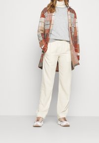 Camisa de cuadros en tonos tierra, sudadera gris, pantalones con cintura elástica crema y zapatillas claras. Texturas suaves y ajuste relajado.