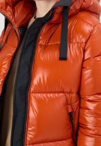 Orange puffer jacket with a shiny finish, featuring a black hood lining, a front zipper, and a side zippered pocket.