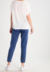 Top blanco de corte holgado y mangas cortas, combinado con jeans de mezclilla azules y zapatillas blancas. Textura suave, diseño casual y ajuste relajado.