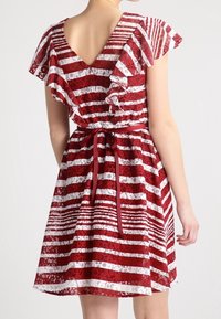 Robe à rayures rouges et blanches en tissu dentelle, manches à volants, dos plongeant en V, et ceinture à la taille pour un ajustement modulable.