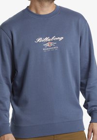 Felpa blu realizzata in morbido misto cotone, caratterizzata da un colletto rotondo, polsini a coste e una stampa grafica con il nome e il logo del brand.